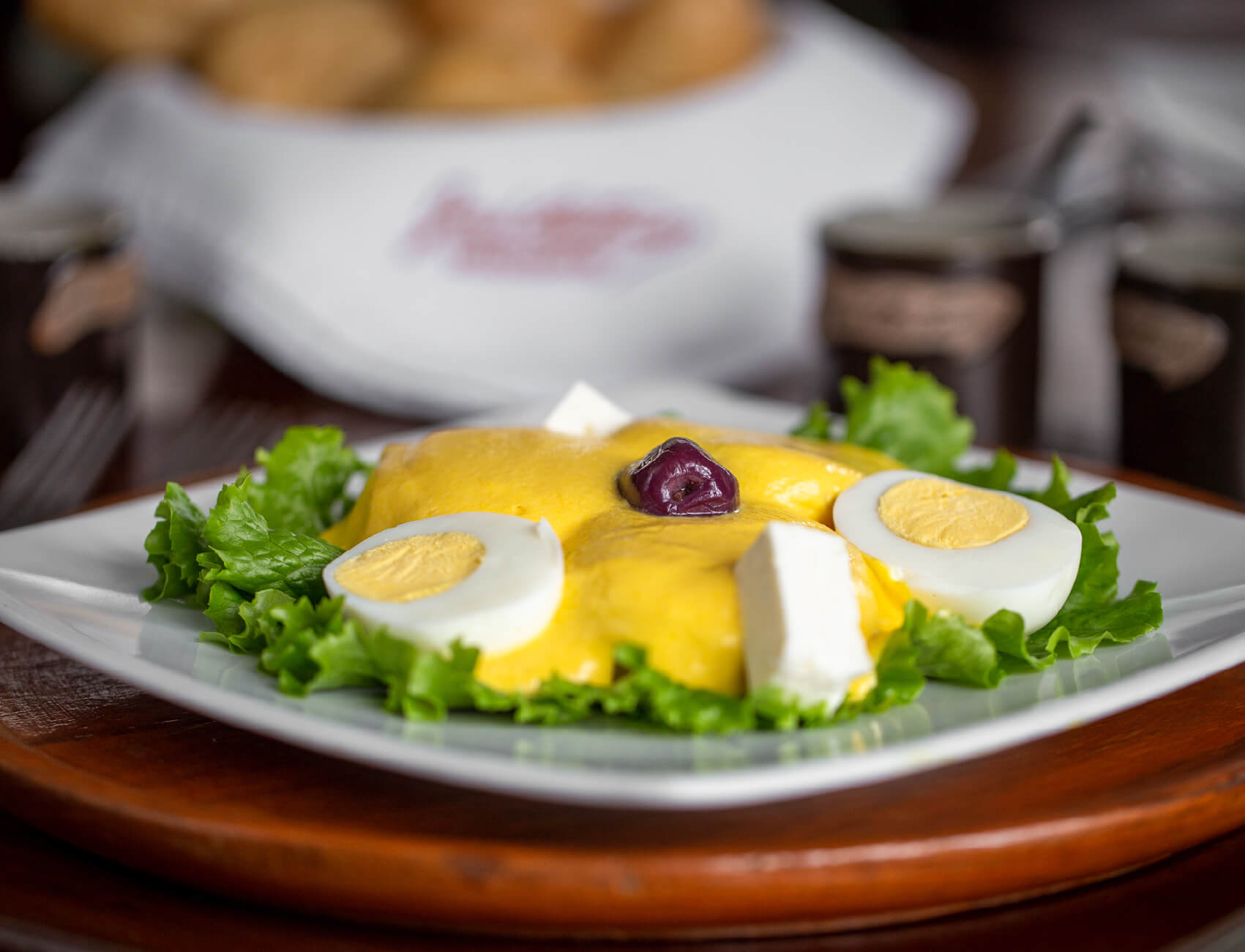 Photo of a plate of papa a la huacaina, garnished with lettuce, sliced hardboiled egg, and an olive.