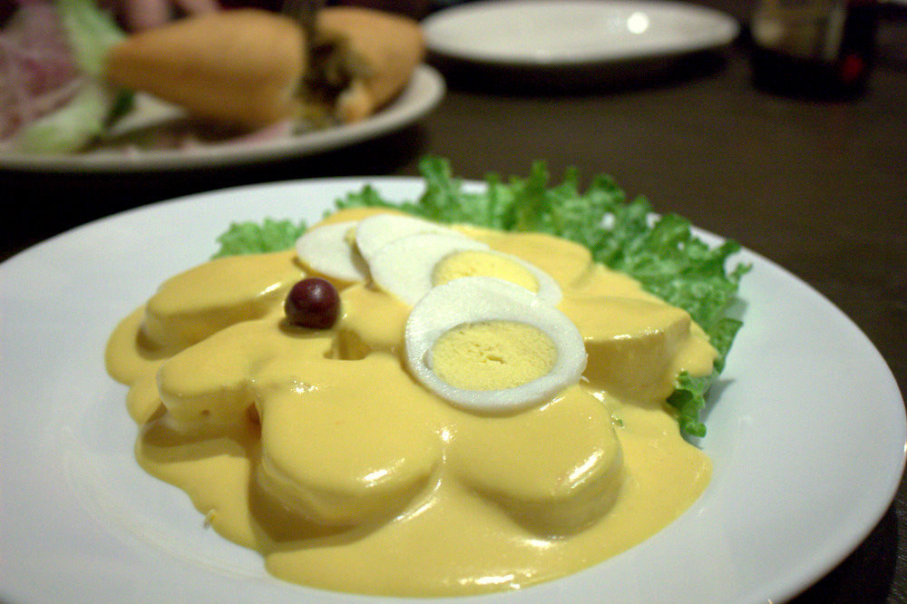 A white plate with the Peruvian papa a la huancaina, a potato and spicy cheese sauce dish.
