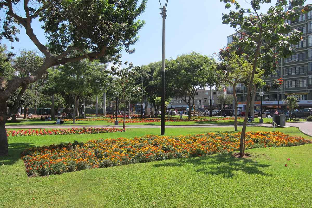 Parque Kennedy's grounds with orange flower beds and trees growing in the green grass.