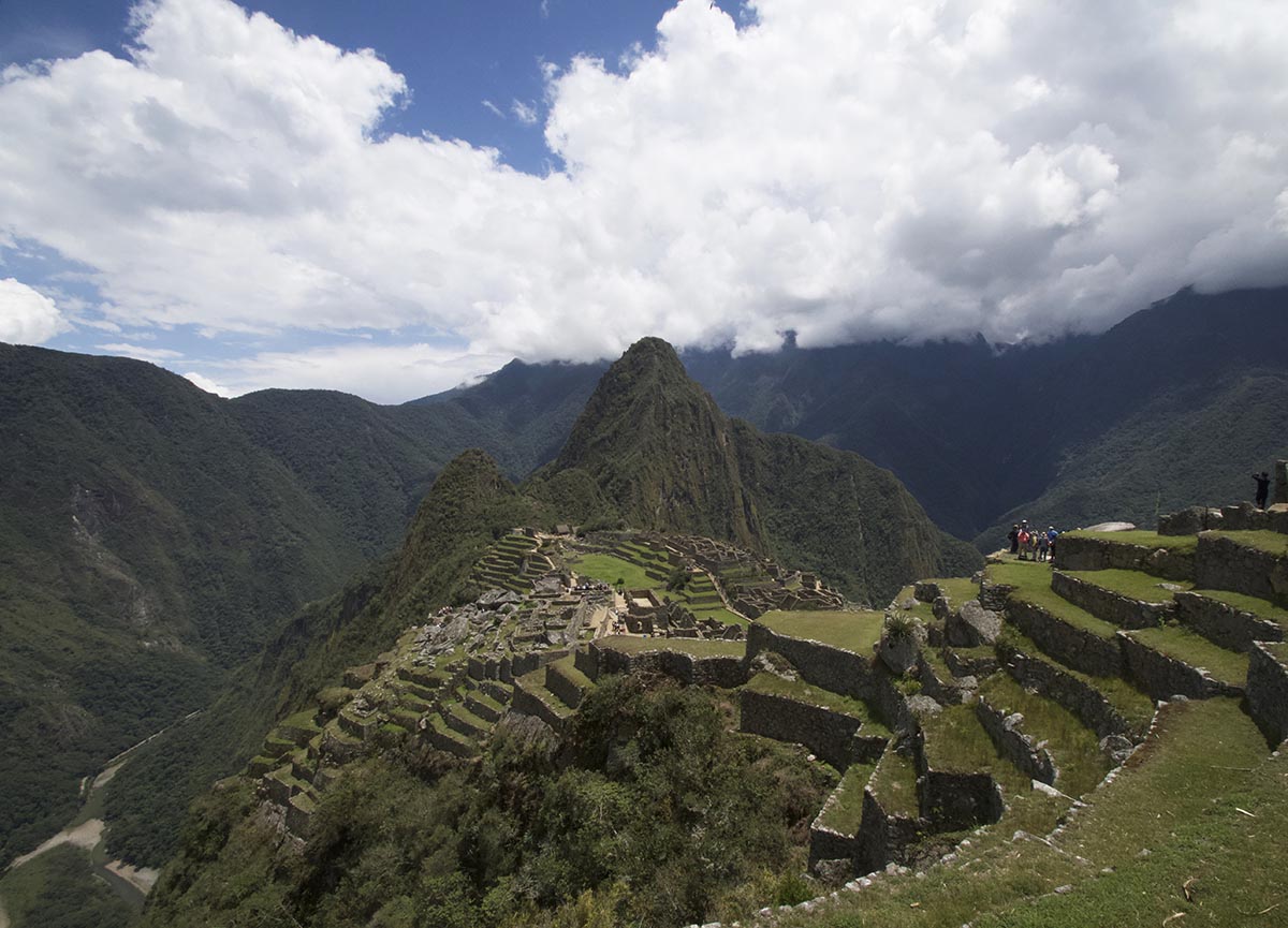 Overlooking the Machu Picchu ruins with Huayna Picchu and high-hanging clouds in the background.