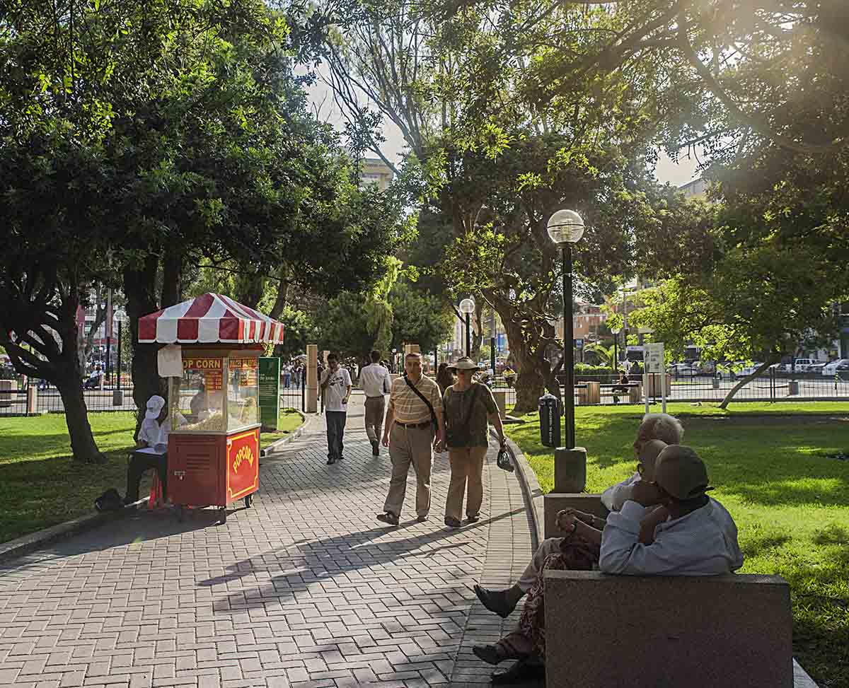 People walking through Parque Kennedy, passing a popcorn vendor and people sitting on benches.
