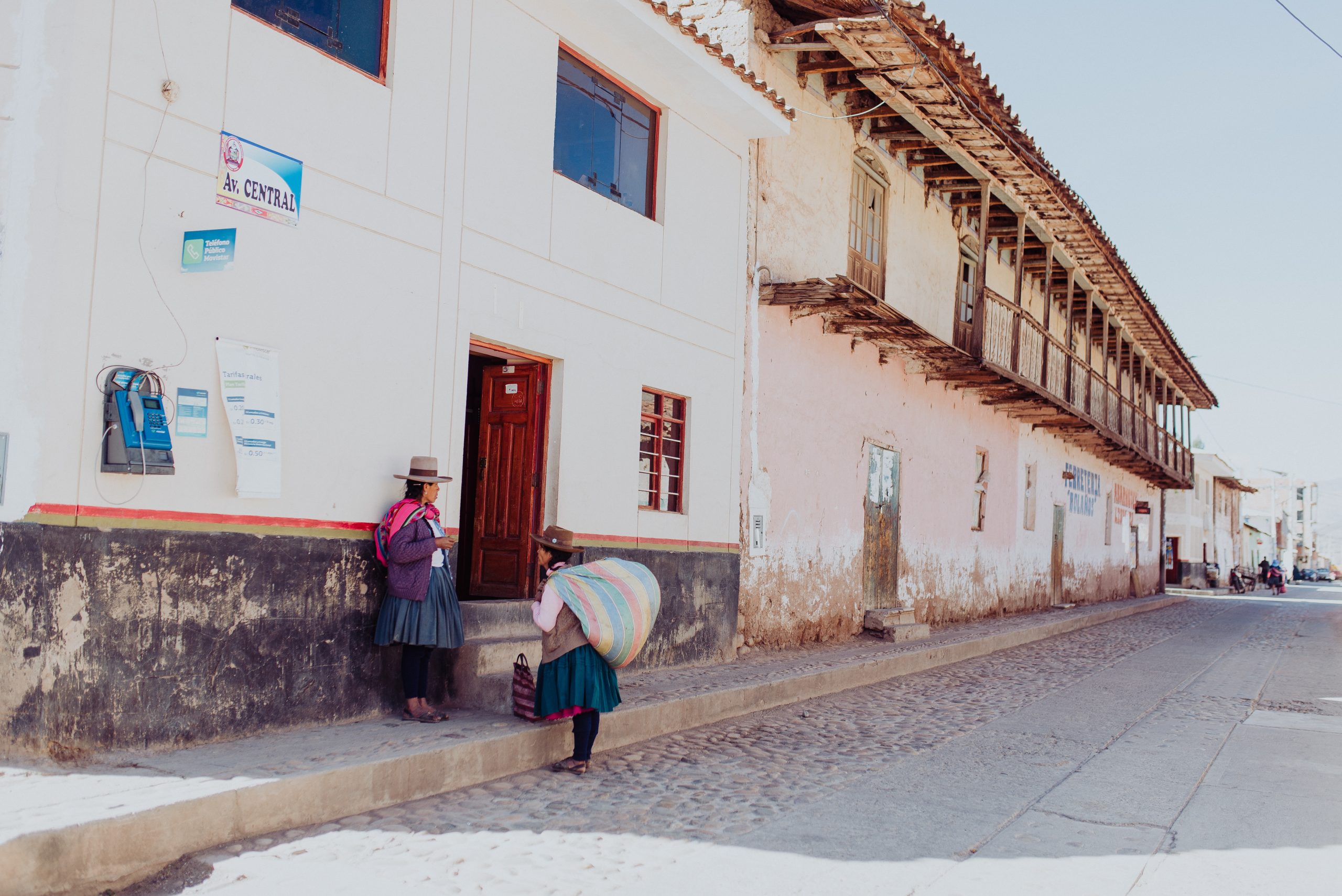 Two women of the Andes region of Peru meeting on a street, holding large bags on their back.