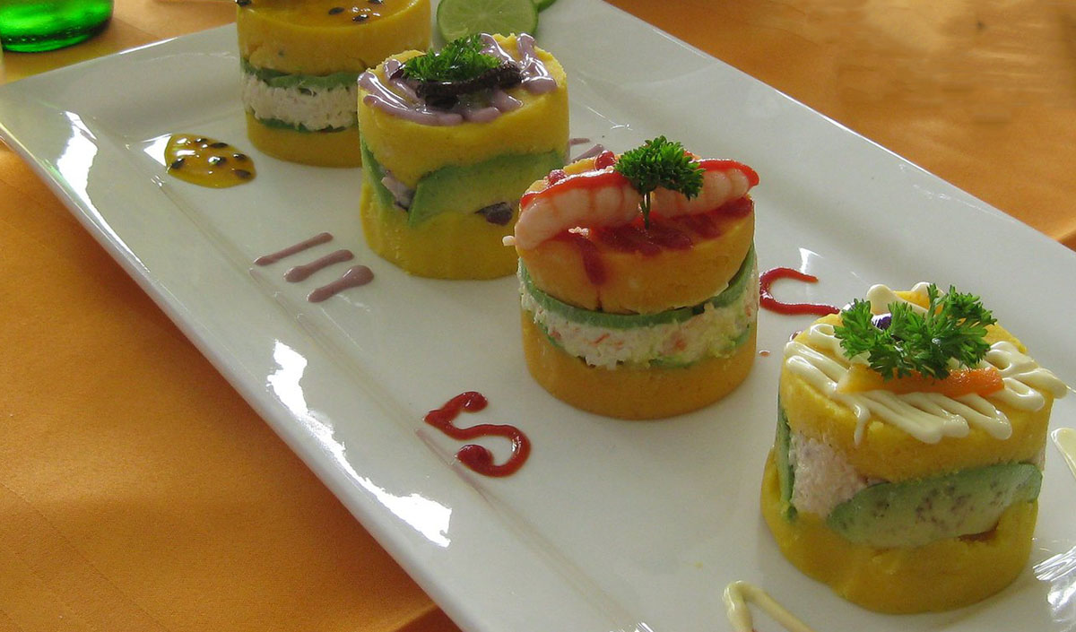 Four styles of garnishes on top of causa rellena appetizers, including mayo, shrimp and olive sauce.