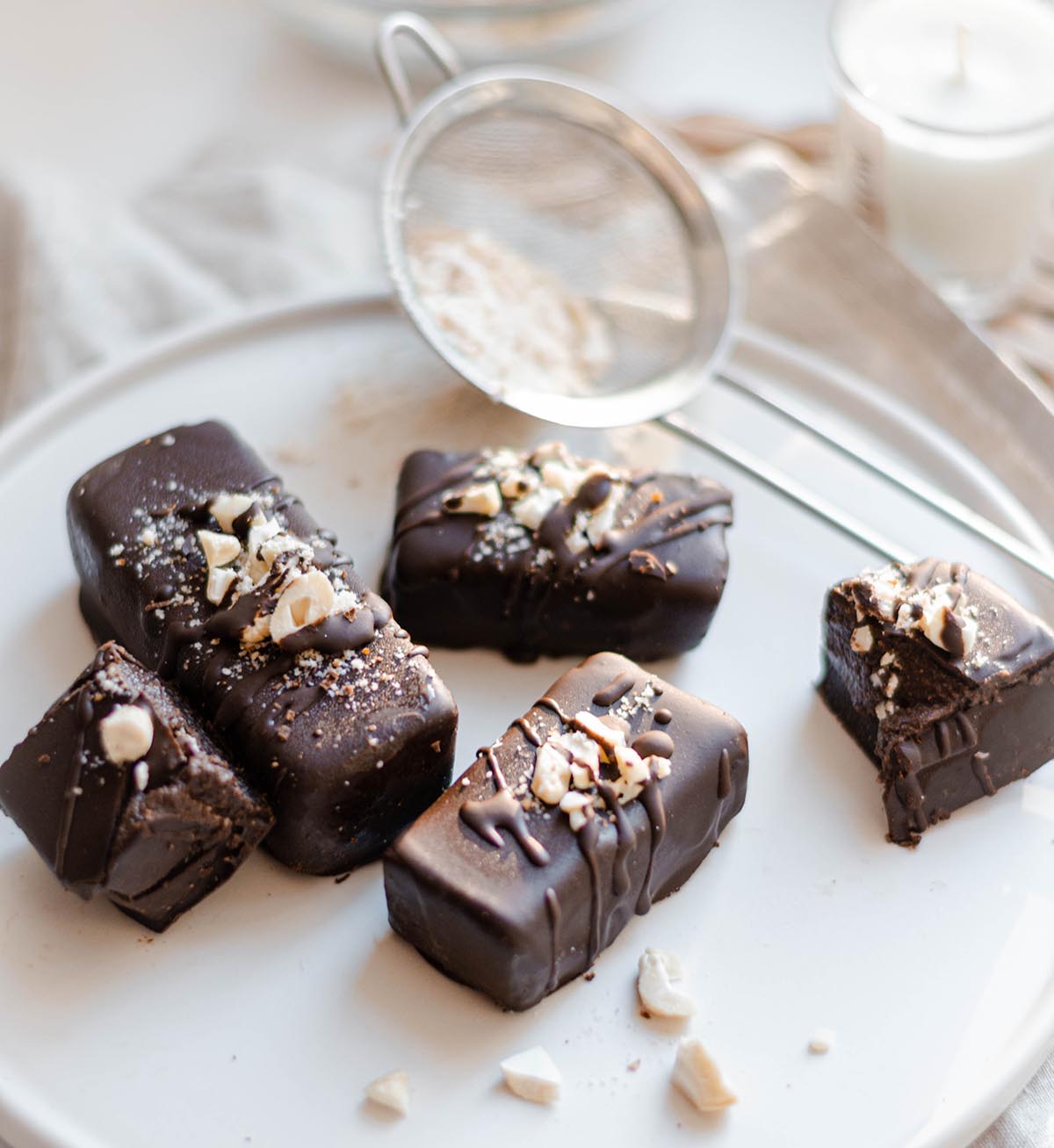 A white plate of rectangular dark chocolate truffles with peanuts and salt sprinkled on top.