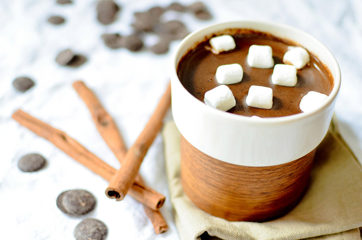 Mug of hot cocoa with marshmallows. Cinnamon sticks and chocolate chips scattered on the table.