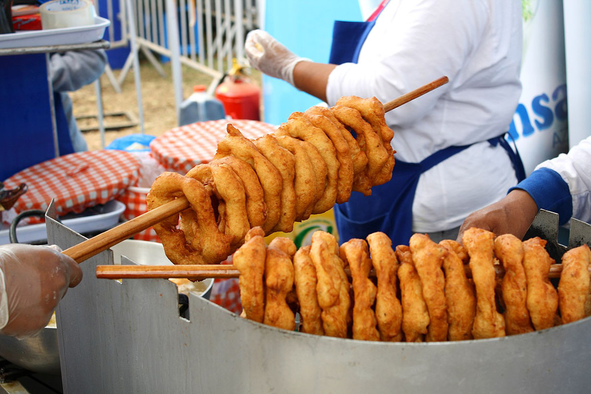 Wooden sticks with many brown doughnuts known as picarones sit above a fryer.