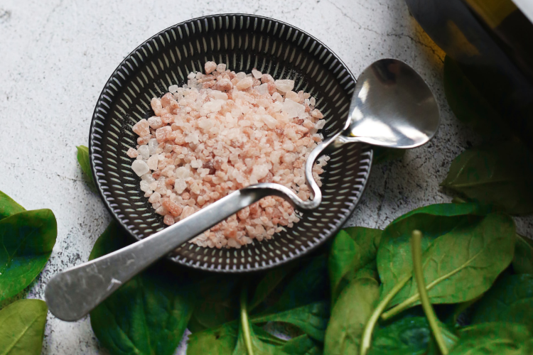A small bowl of Peruvian pink salt with basil leaves and an olive oil bottle to the right