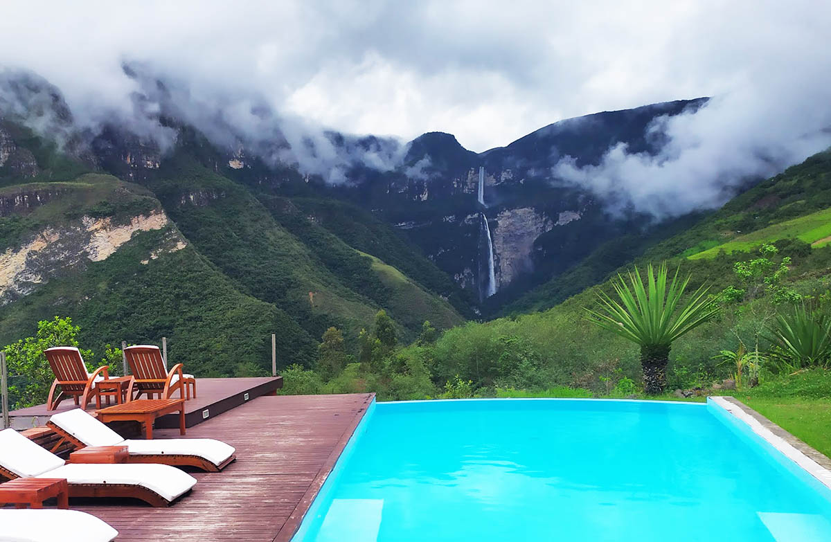 A turquoise pool surrounded by jungle landscape and the Gocta Waterfall in the distance.