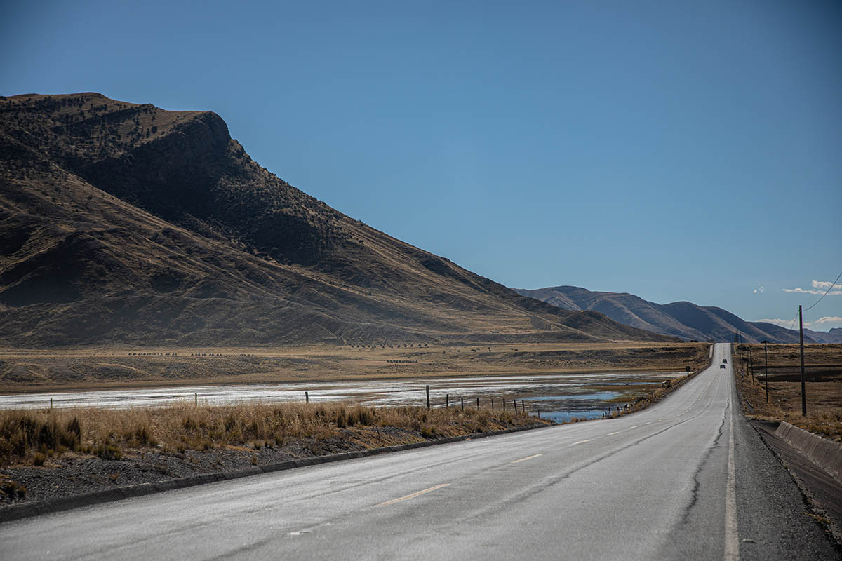 Empty, grey road with mountains and blue sky in the distance.