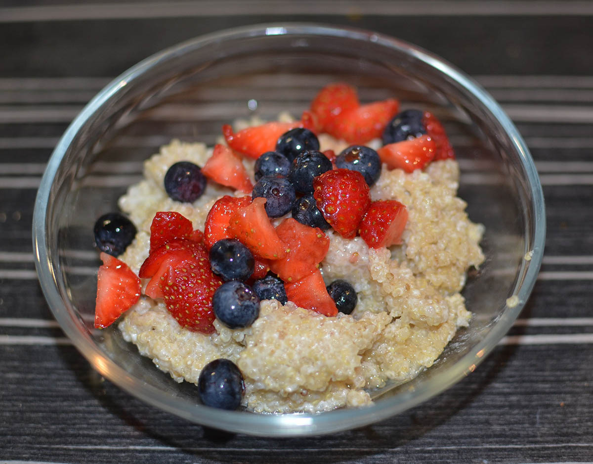 Cooked white quinoa in a glass bowl with strawberries and blueberries.