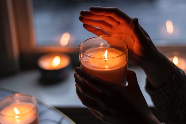 foreground hands holding a candle and background 3 additional candles on a windowsill