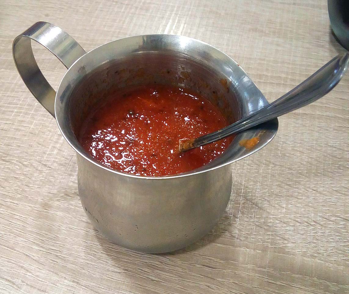 Red rocoto hot sauce in a silver cup with a handle and silver spoon.