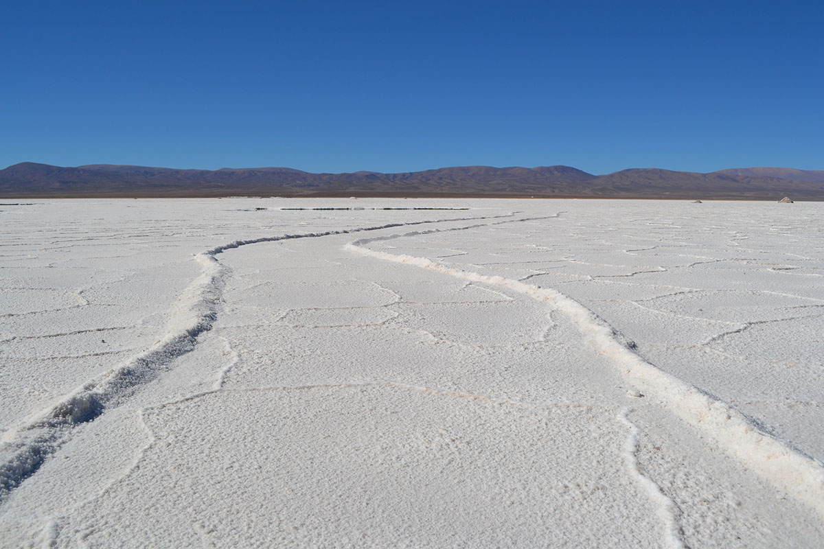 White salt stretches to dark, shallow hills under blue skies in the Salinas Grandes of Argentina.