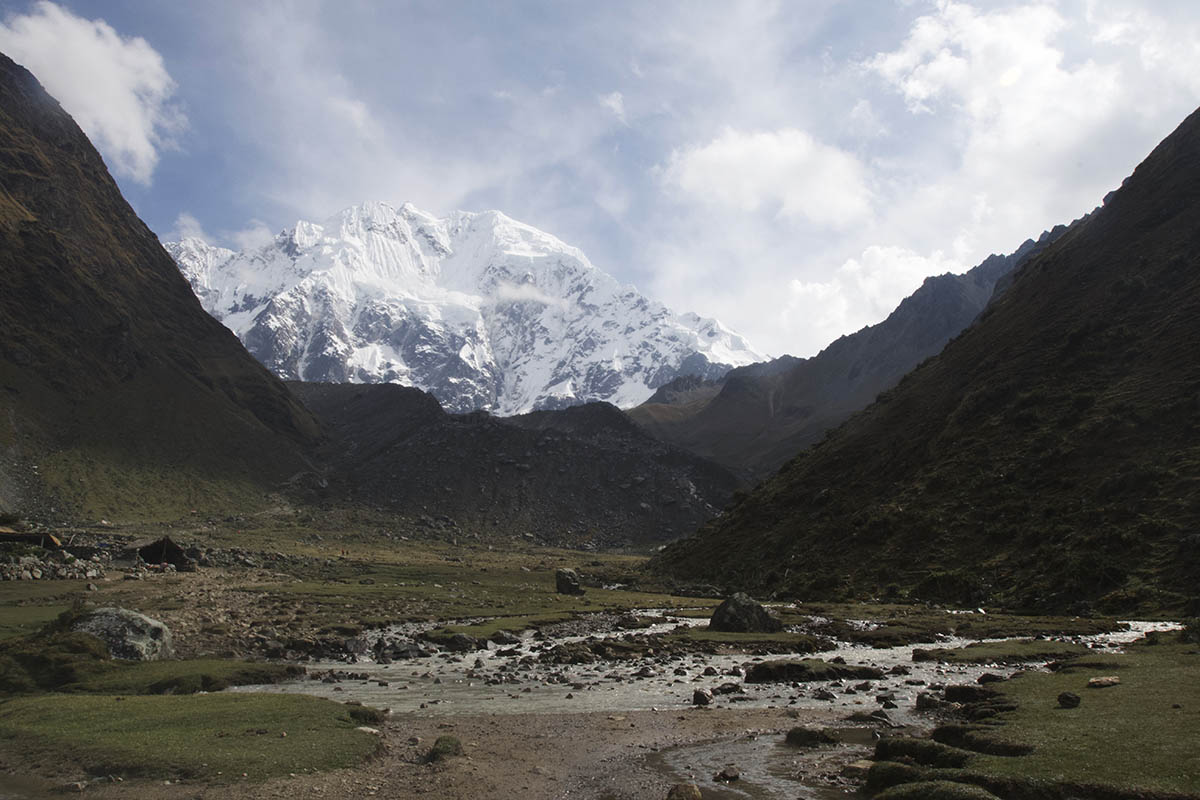 Snow covered mountain in the distance behind brown and green hills on the Salkantay trail.