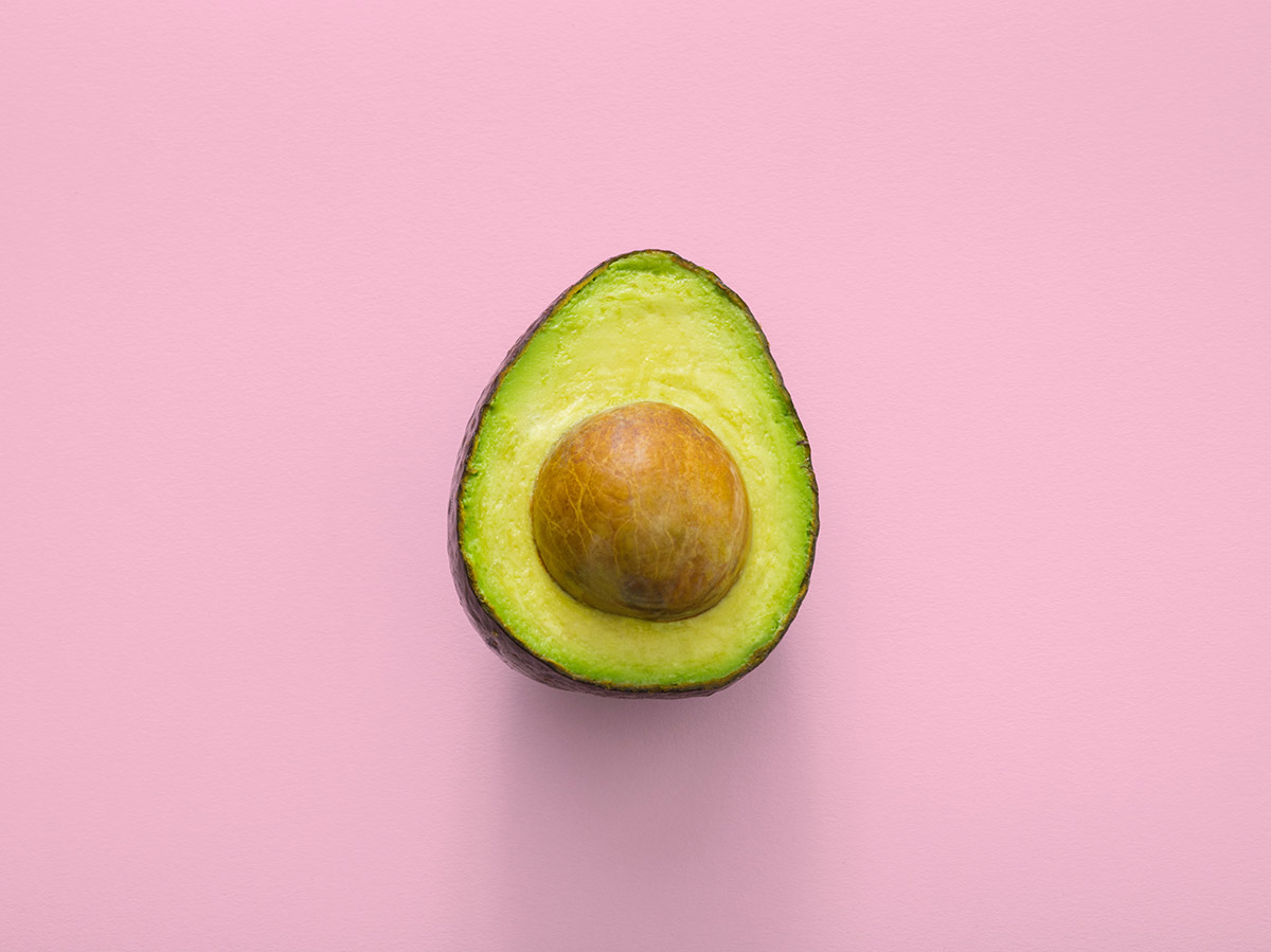 A sliced green avocado with the seed against a pink background.
