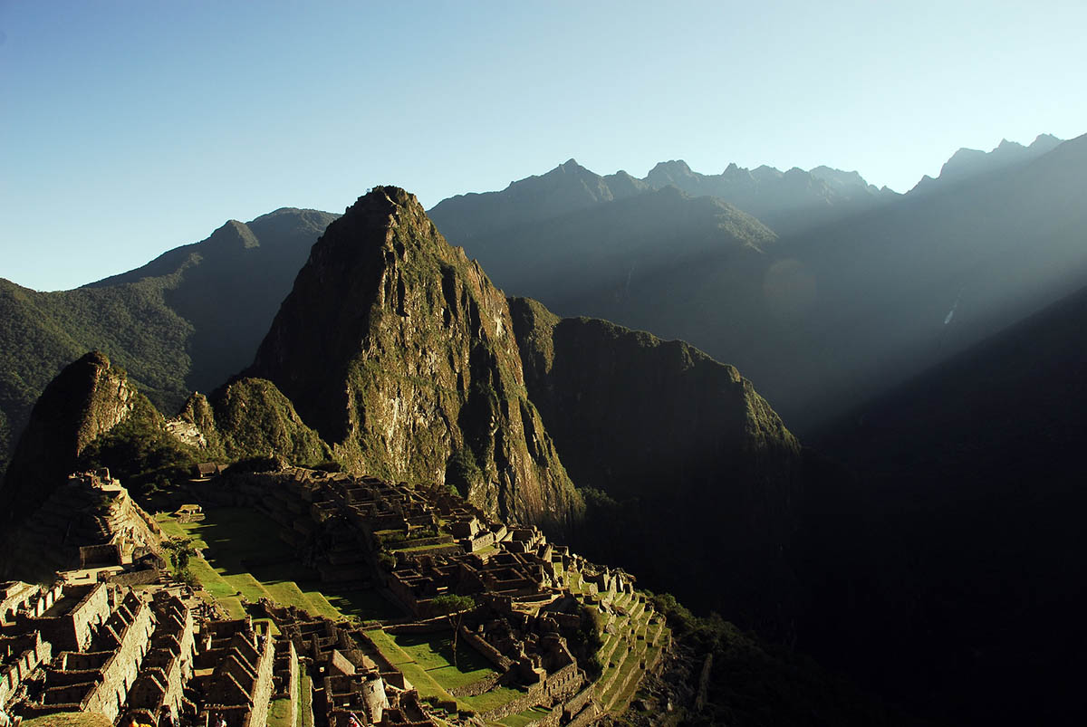 Soft sunlight illuminates the side of the Machu Picchu ruins at sunrise.