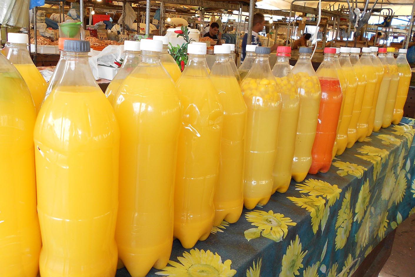 Many large plastic bottles full of yellow tucupi sauce. Food market in background.