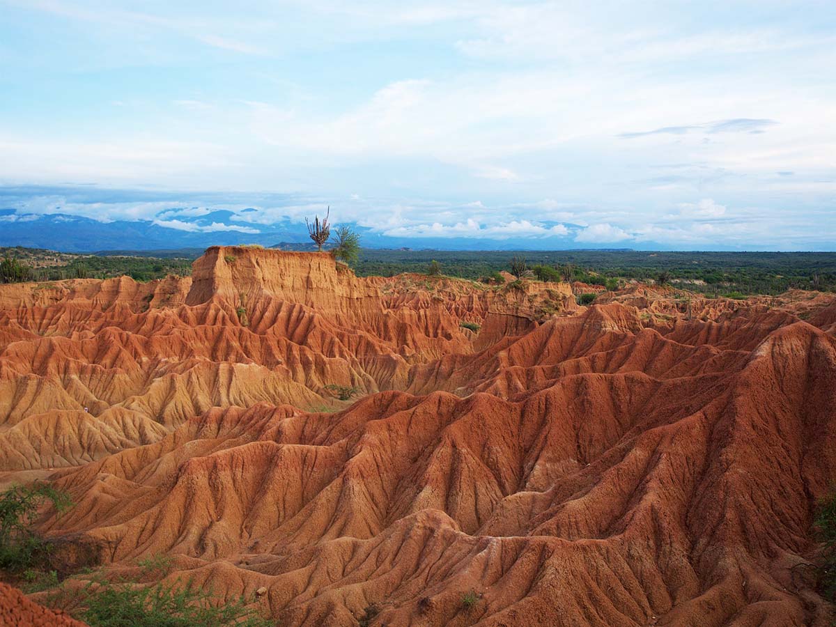 Orange, wavy rock formations and sand sit under a blue, cloudy sky.