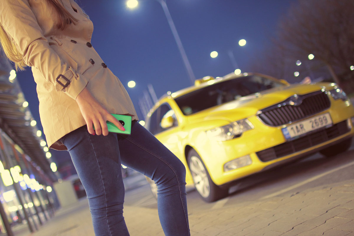 Woman standing outside with blurred yellow taxi in background.