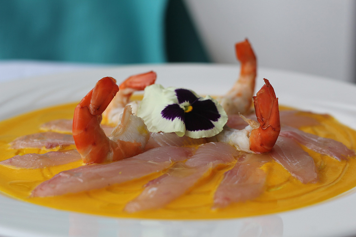 A plate of thinly slices fish with an orange citrus sauce and shrimp on top.