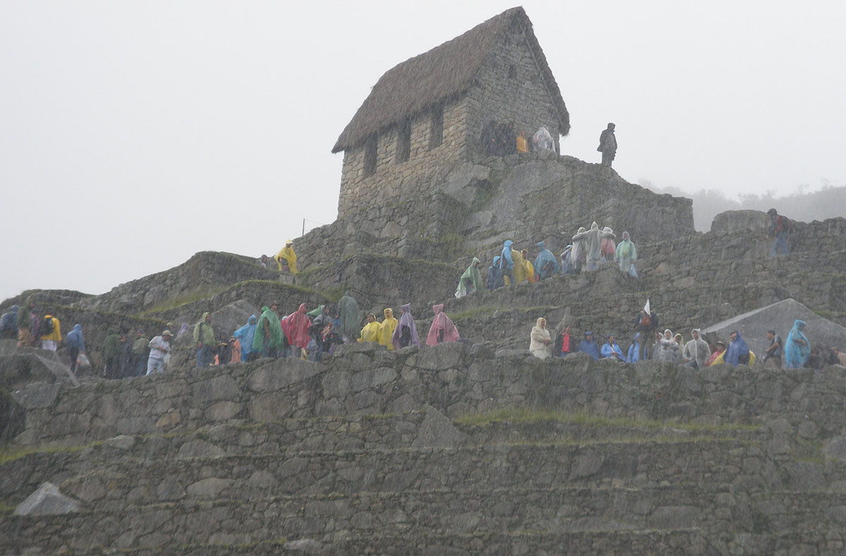 Visitors in colorful ponchos dot the Machu Picchu ruins in the rain and fog.