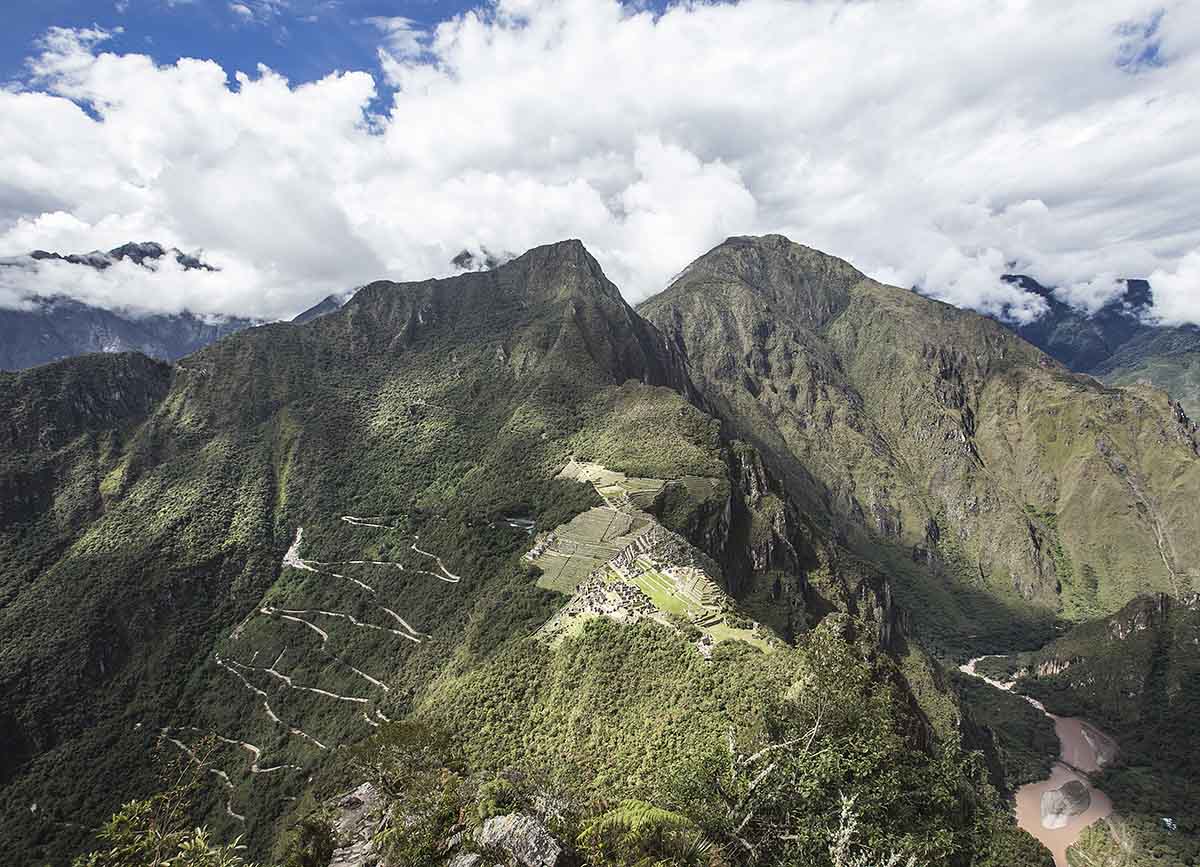 Aerial view of Machu Picchu from Huayna Picchu. Cloudy skies and green mountains surround the site.