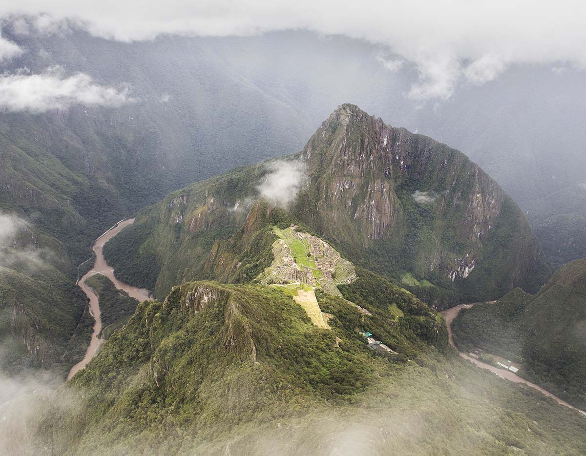 Machu Picchu ruins and Huayna Picchu peak. Clouds pour in from all angles, blurring the view.