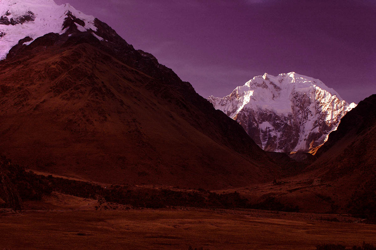 Red tinted ground with snow covered mountains in the distance and a purple tinted sky.