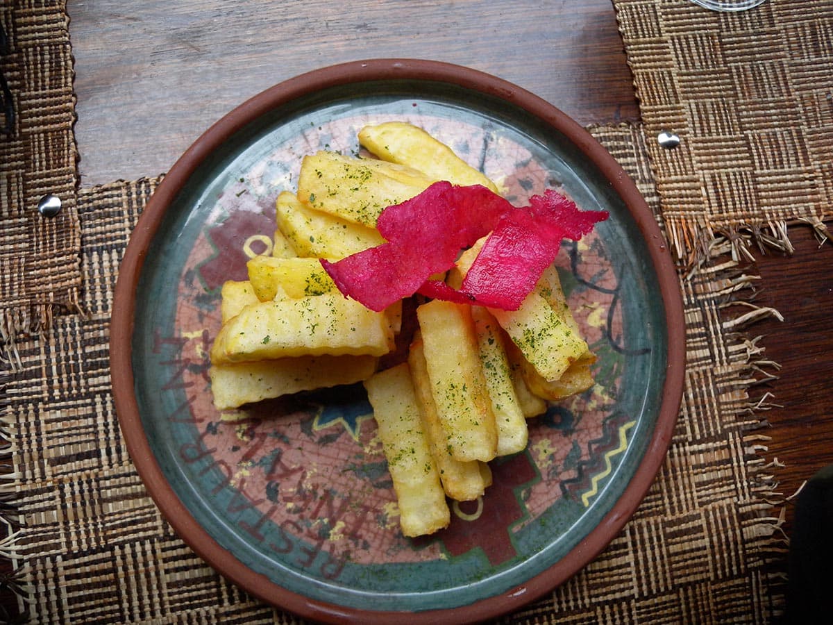 Golden brown deep fried yuca with a red garnish on a glazed brown and blue ceramic plate.